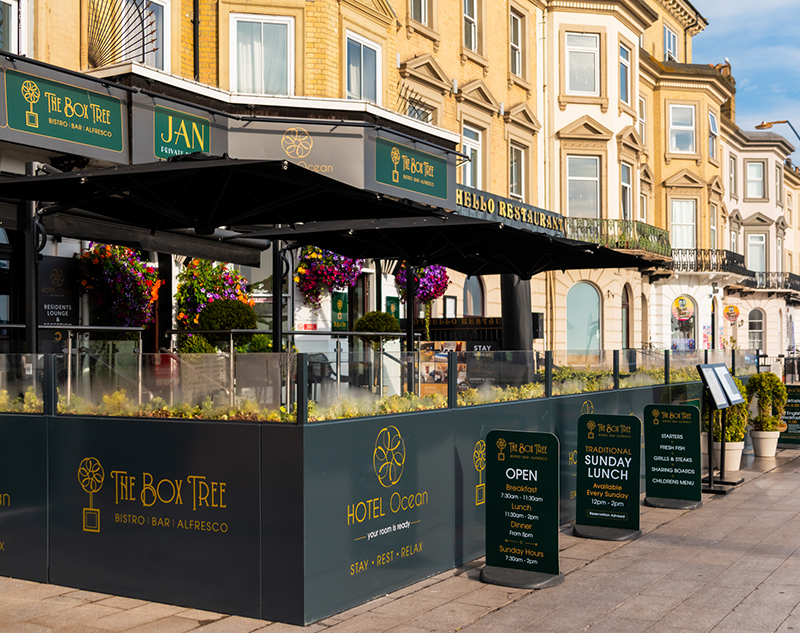 External view of the alfresco dining area at The Box Tree bistro with branded screens and parasols